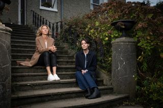 Eve Best and Suranne Jones sit on the steps of a large house next to an overgrown hedge