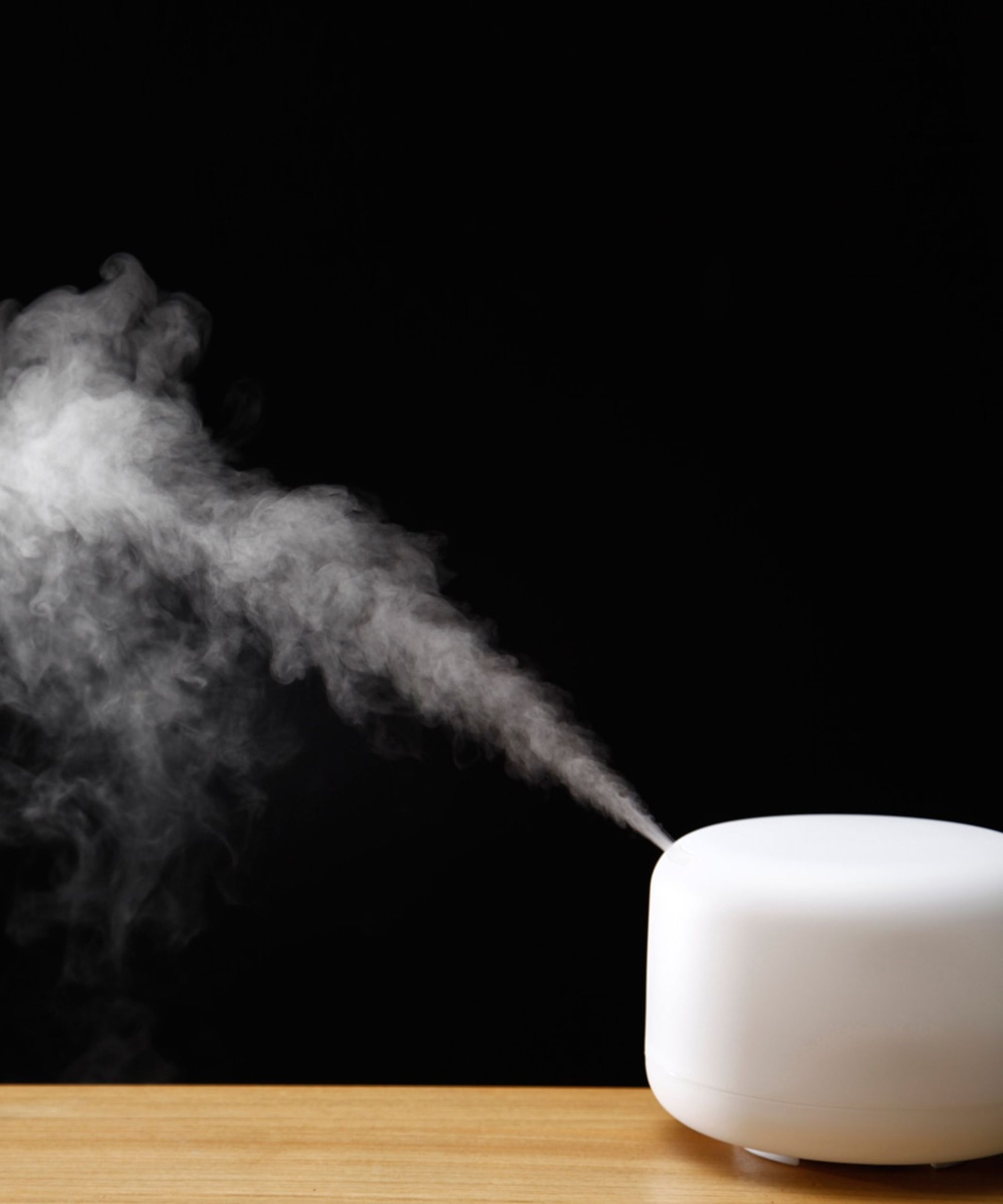 White MUJI diffuser on a wooden counter with a black background