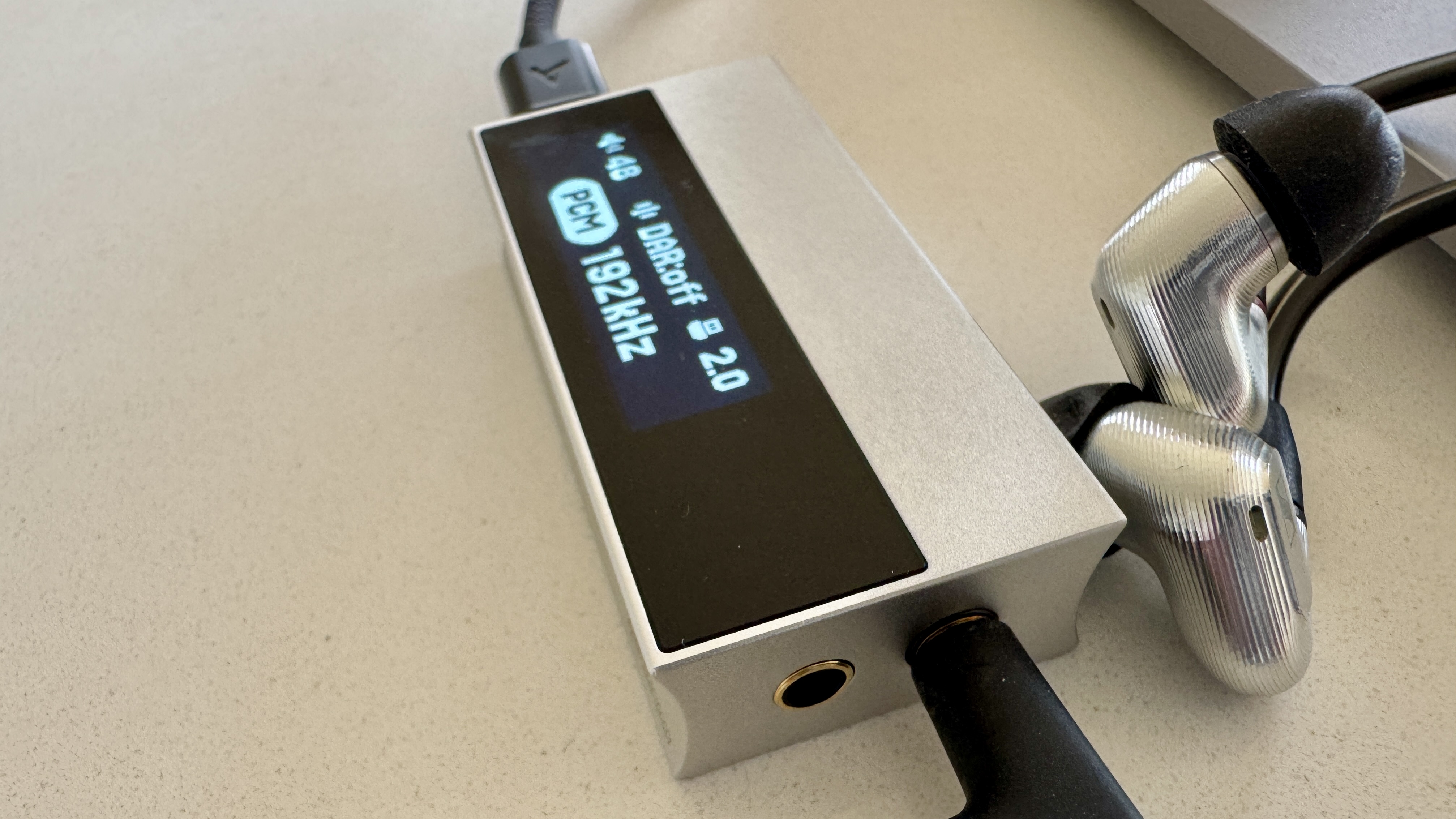 The Astell & Kern AK HC5 on a grey table, with the top plate illuminated and hooked up to Sennheiser IEMs and a FiiO digital audio player