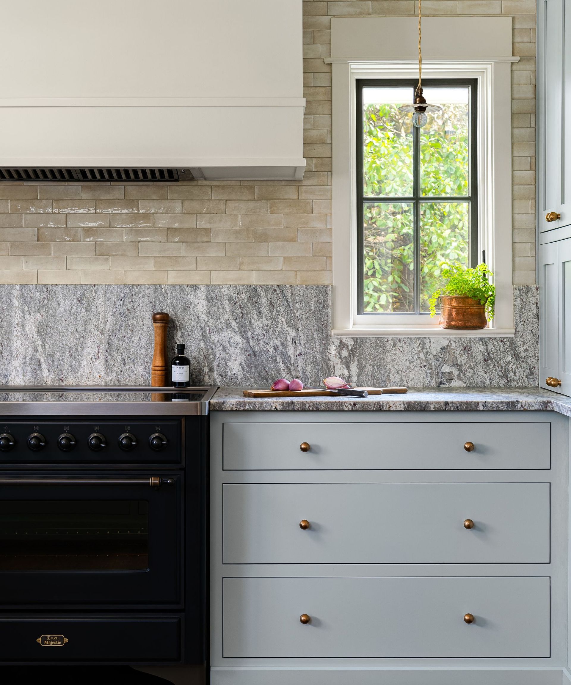 A kitchen with light blue cabinets, gray marble countertops, beige tiles, and a black range cooker