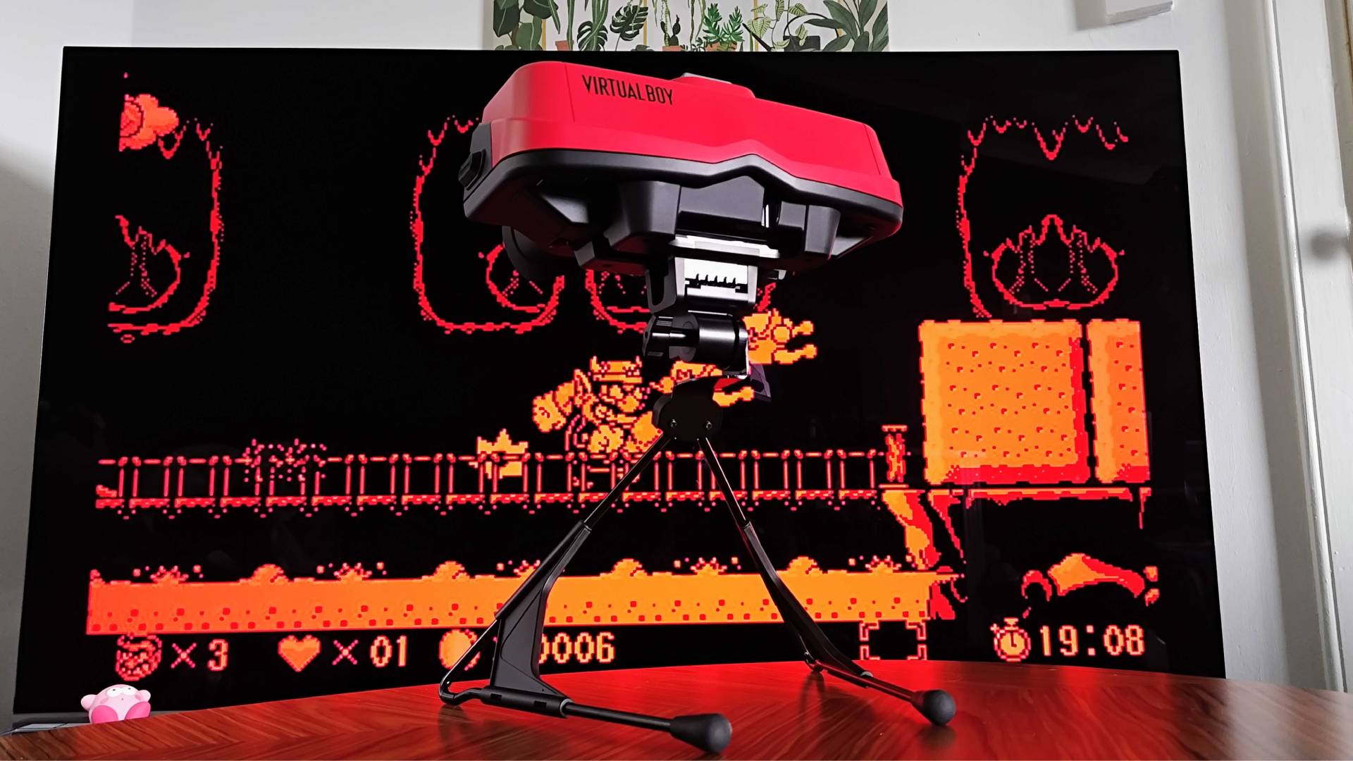 Switch Virtual Boy on woodgrain table with TV in backdrop and Virtual Boy Wario Land on screen.