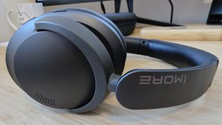 A pair of dark grey and black 1More Sonoflow headphones sitting on a wooden table