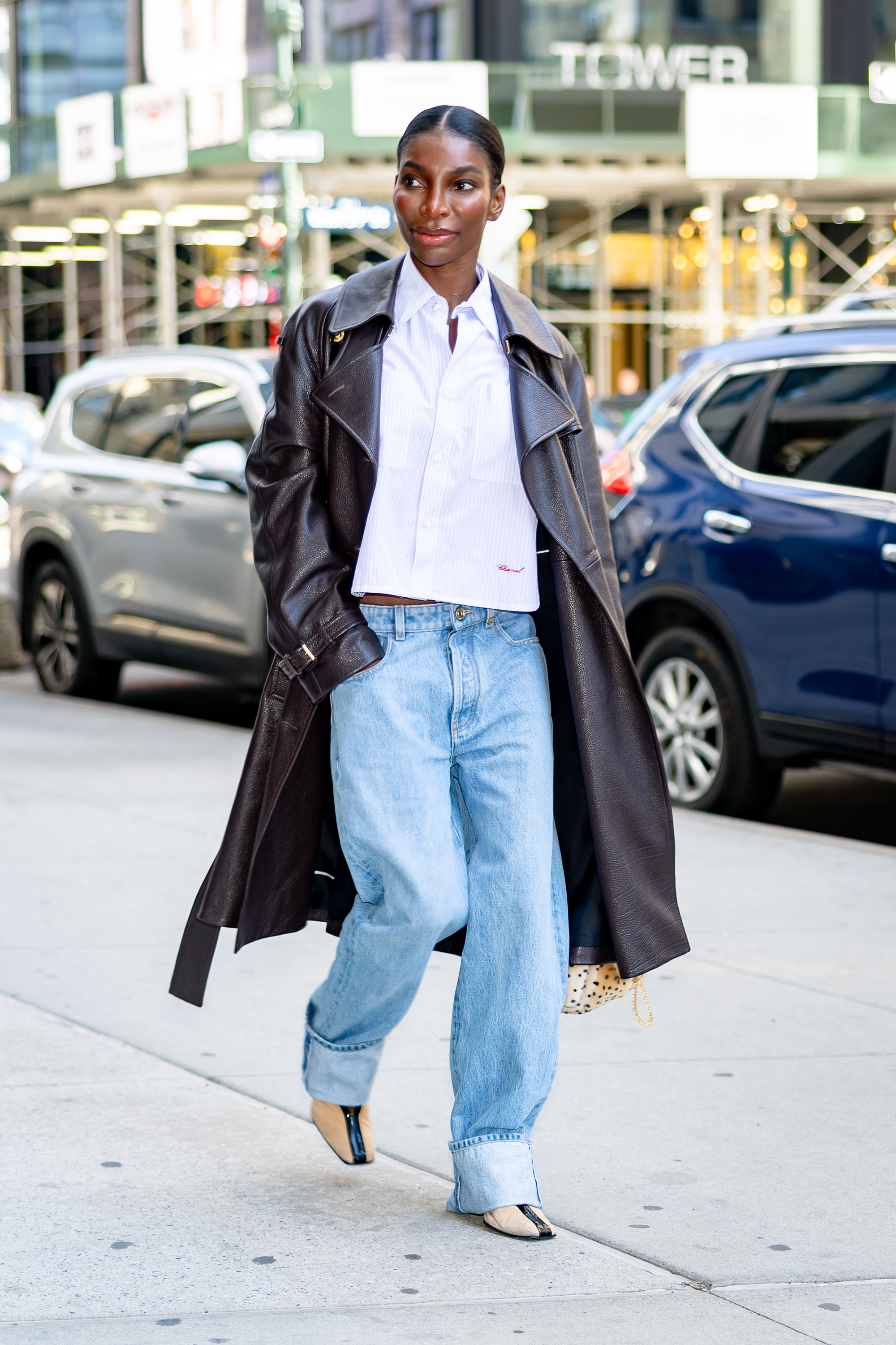 Michaela Coel walks down the street in New York wearing low-rise cuffed jeans with a white shirt, a leather trench coat and Chanel's high-vamp pumps.