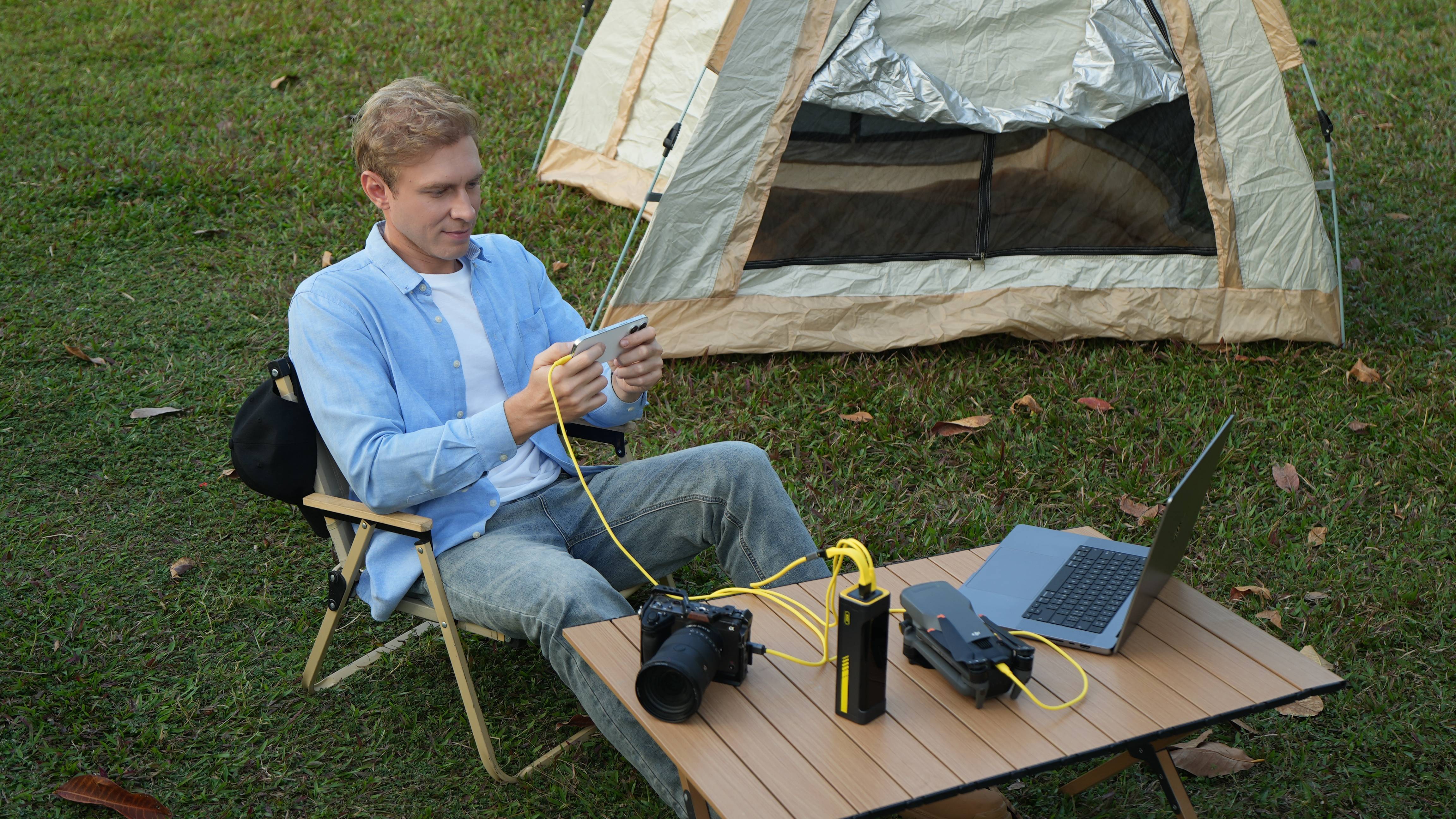 AOHi Starship 240W Power Bank being used to power three devices by man sitting next to tent