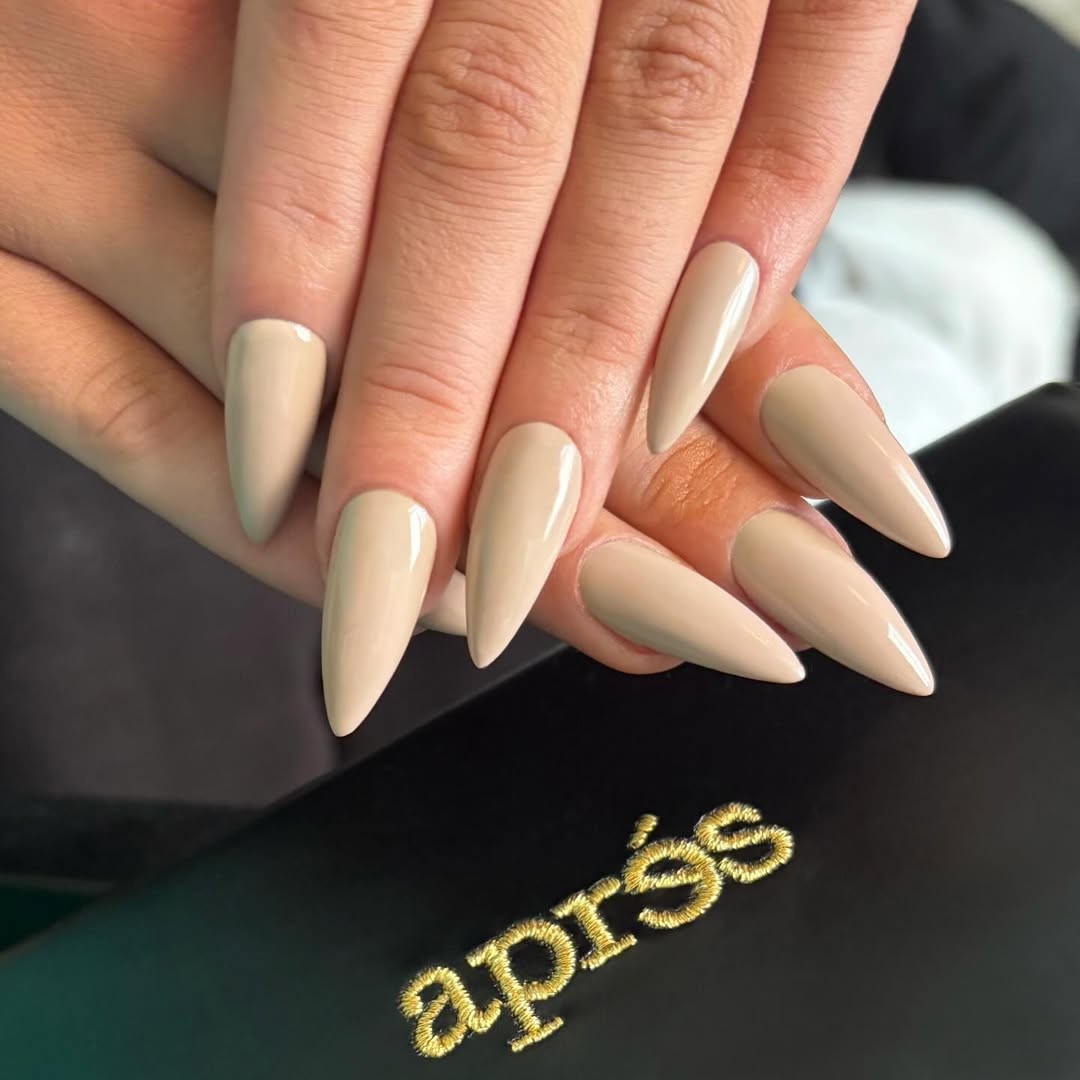 A hand with an almond-shaped nude manicure.