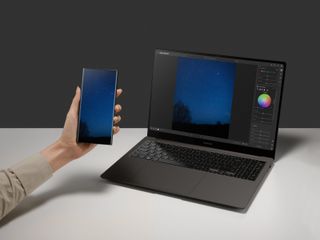 Samsung Book3 Ultra laptop on desk, with phone held beside it