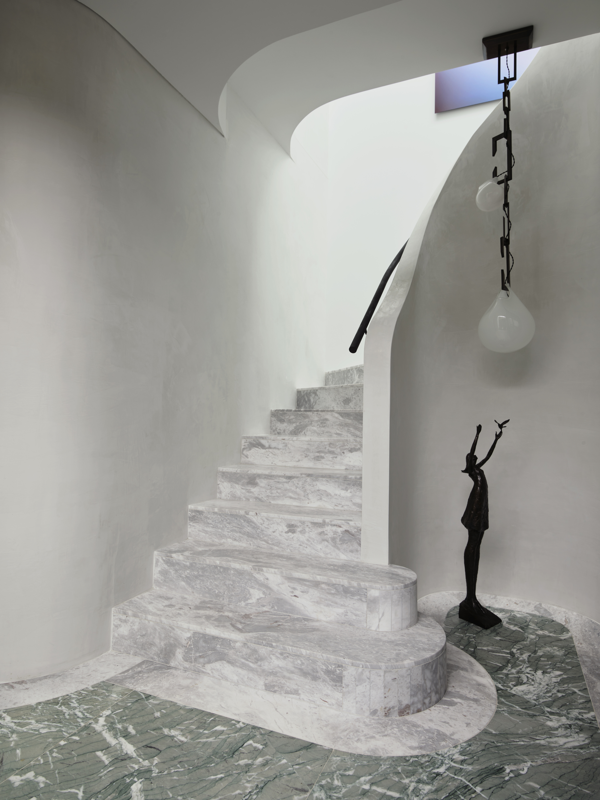 entryway with green marble flooring and white marble curved staircase with a sculpture reaching up to a pendant light and curved walls