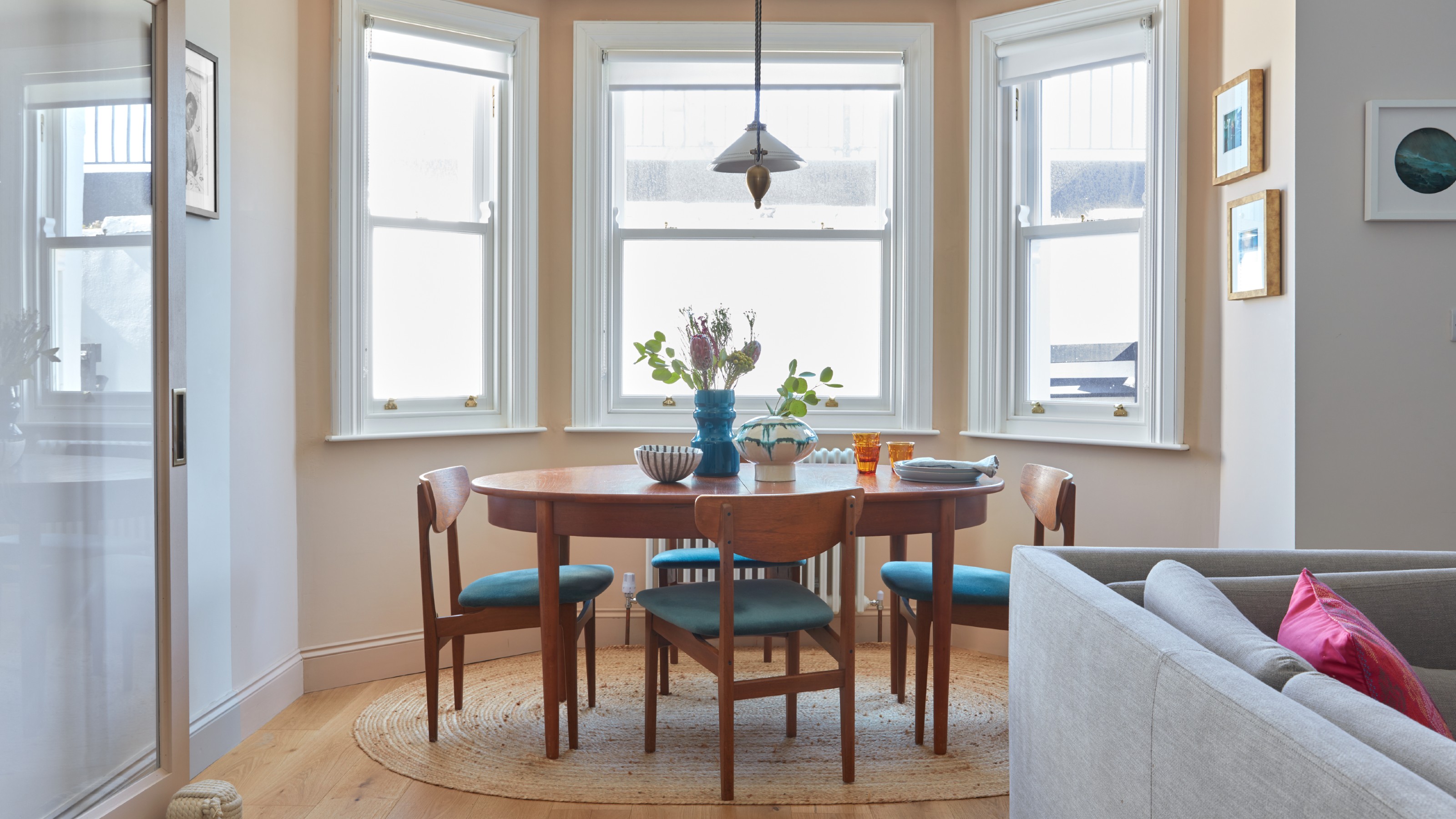 A dining area in a living room with an oval midcentury table and matching chairs on top of an oval jute rug