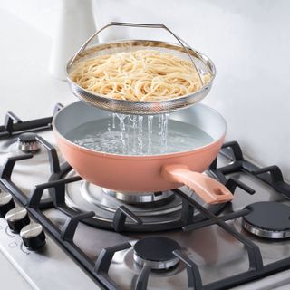 Dusty pink pan boiling pasta on top of stove