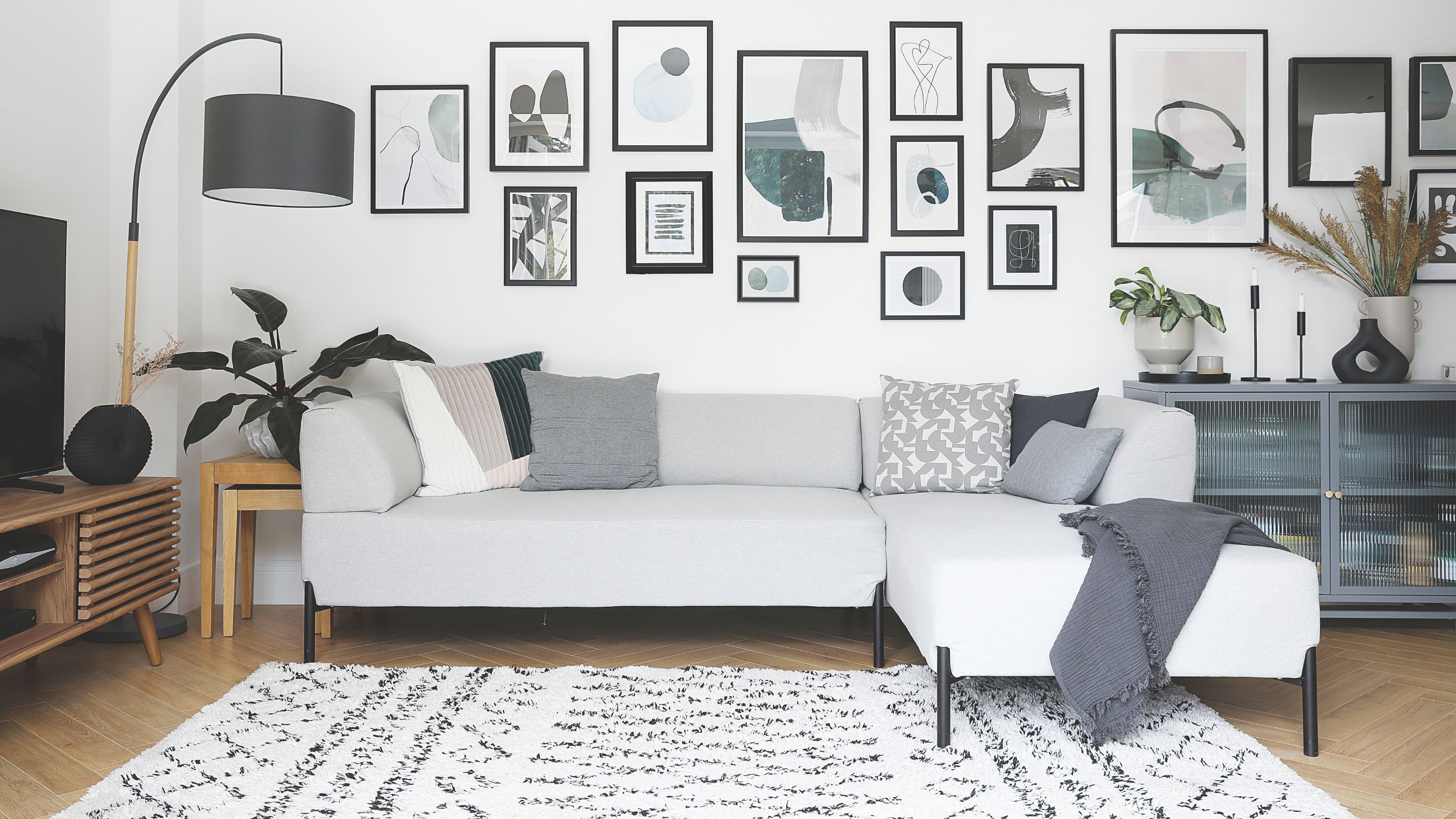 White painted living room with a grey sofa and cushions, a white and black rug, and a gallery wall 