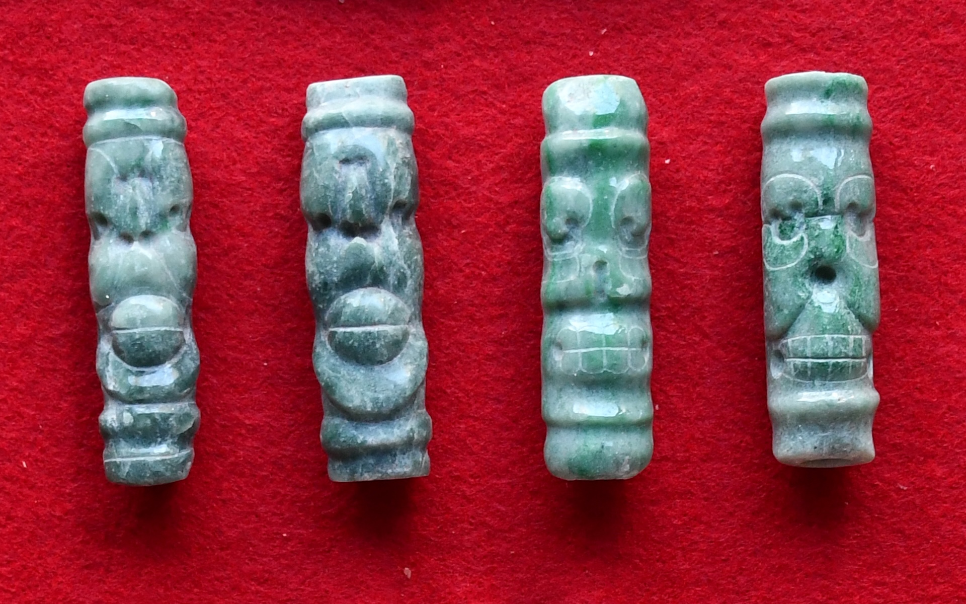 four tube-shaped beads carved from jade against a red background
