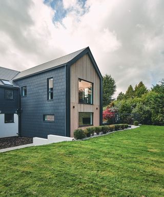 tall contemporary home with wooden panelling and grey tiles seen from the rear view showing garden and trees