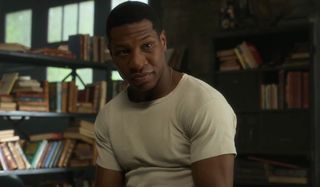 Jonathan Majors sits in front of shelves stocked with books in Lovecraft Country.