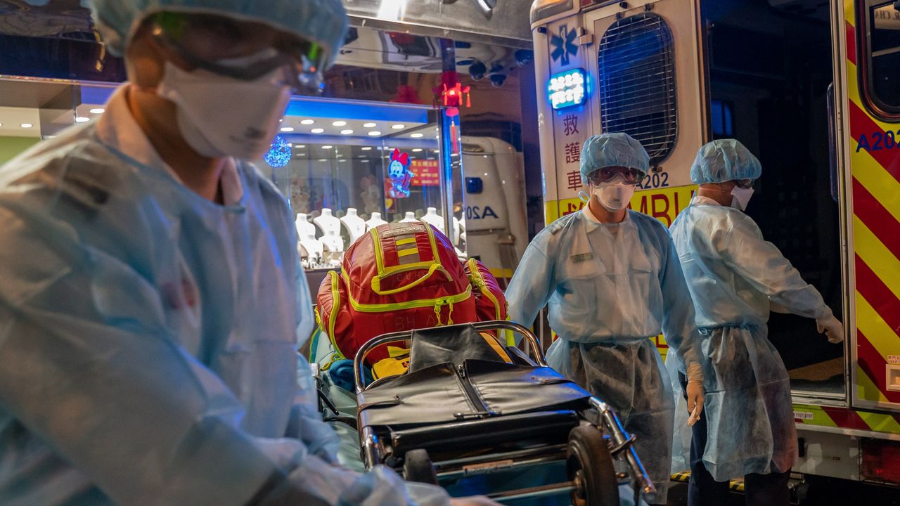 Paramedics wearing personal protective equipment carry a stretcher off an ambulance.