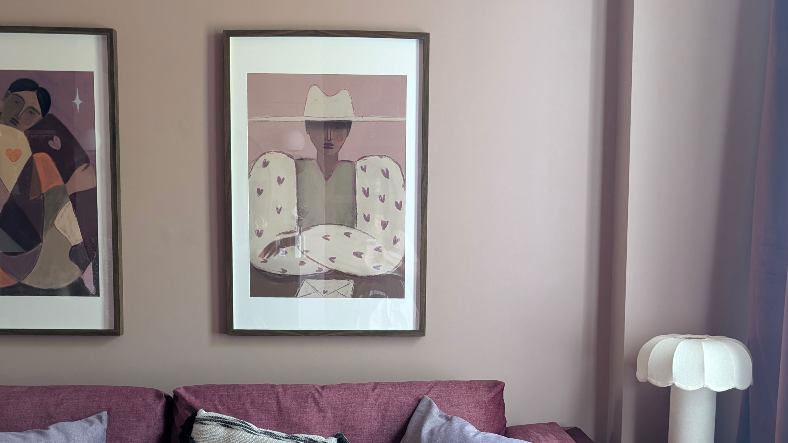 Pale pink living room with framed paintings of cowgirls on wall above dark pink sofa