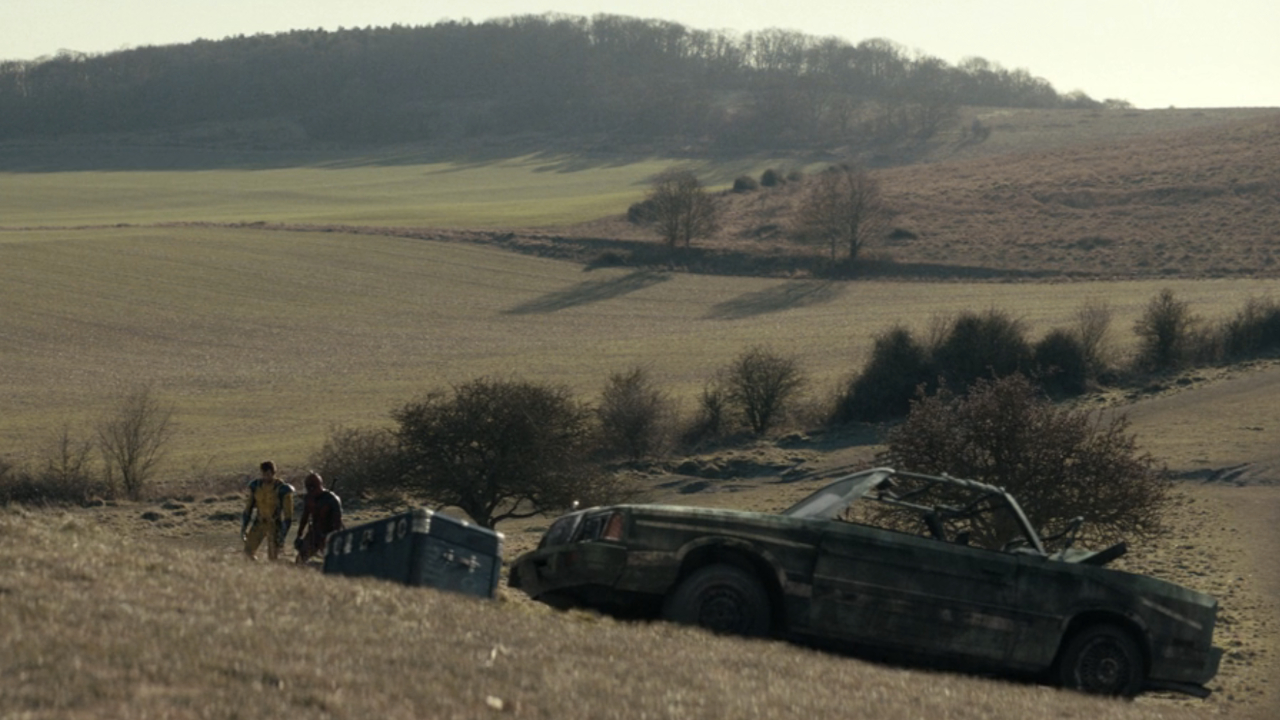 Deadpool &amp;amp; Wolverine walk in The Void near a burnt out car.