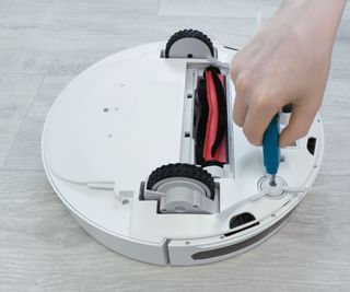 Someone using a screwdriver to open up the bottom of a white robot vacuum cleaner