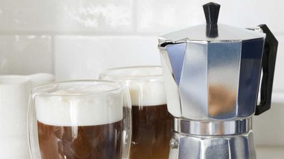 Stovetop espresso maker and two cups of coffee on kitchen worktop