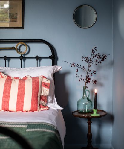 detail of an antique bed with striped cushion and bedside table with candle and glass jar