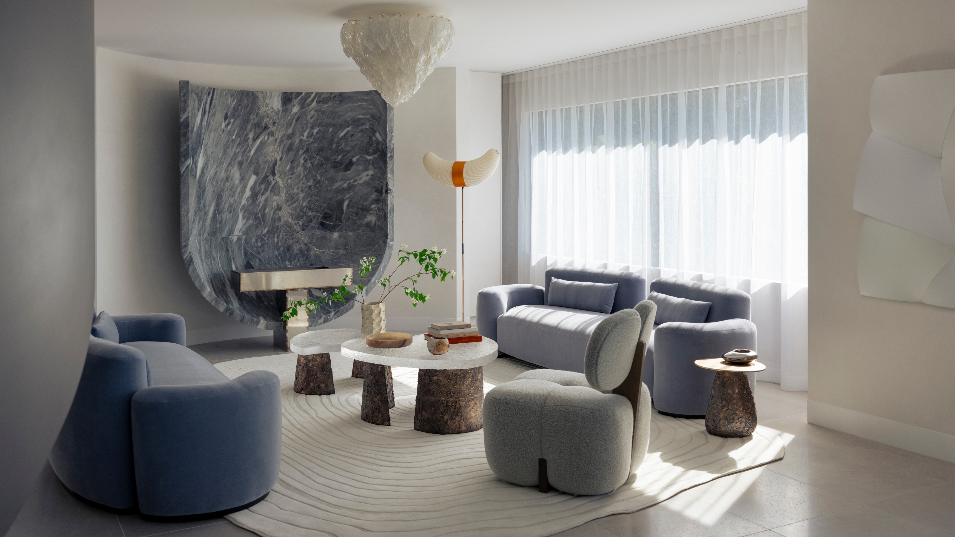 Image of a white living room with light velvet blue sofas and a large abstract blue art piece on the back wall. There is a brown and white nesting coffee table in between the two blue sofas.