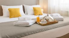 A mattress in a hotel made up with pillow and sheets, with folded towels and a breakfast tray on top of the bed