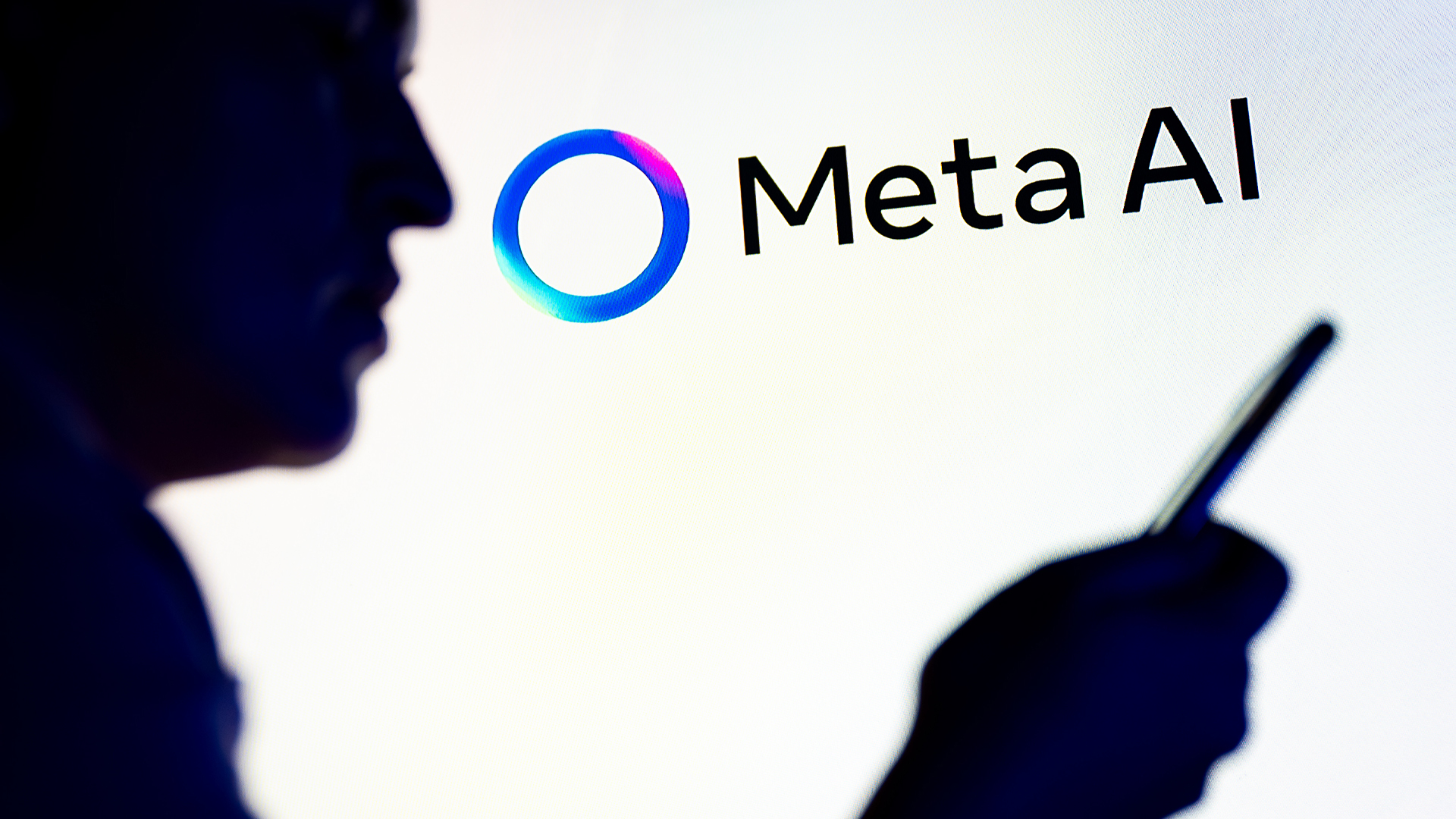 Meta AI logo and branding pictured on a wall with silhouette of man holding up smartphone in foreground.
