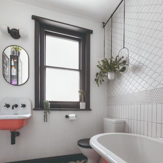 A white bathroom with a contrasting black window frame and hanging plants on a rail