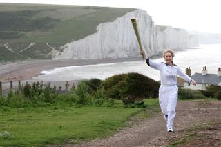 Kathy Gore runs with the Olympic Flame at Seaford Head, with a view of the Seven Sisters cliffs in East Sussex.