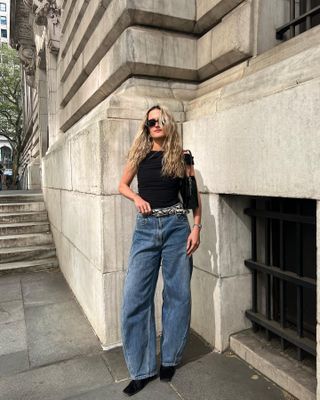 Editor Eliza Huber wearing black tank top, snakeskin belt, and blue barrel jeans.