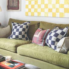 A living room with a green sofa and chequered scatter cushions matching the chequered painting hanging above