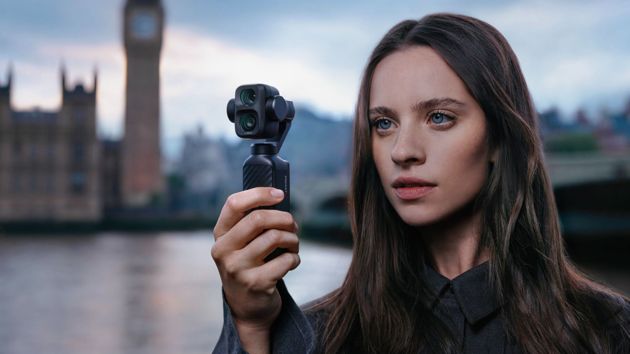 A young woman holding a DJI Pocket Osmo 4P in front of the houses of parliament in London