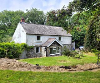 A stone cottage surrounded by trees and a small driveway to the side