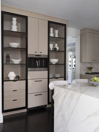 A neutral kitchen with a marble island and large display cabinets with black trim