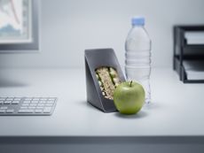 sandwich, bottled water, and green apple on an office desk with a monitor and paper tray in the background