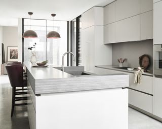 A modern kitchen with an island with black Vermont worktop, white cabinetry and burgundy leather chair