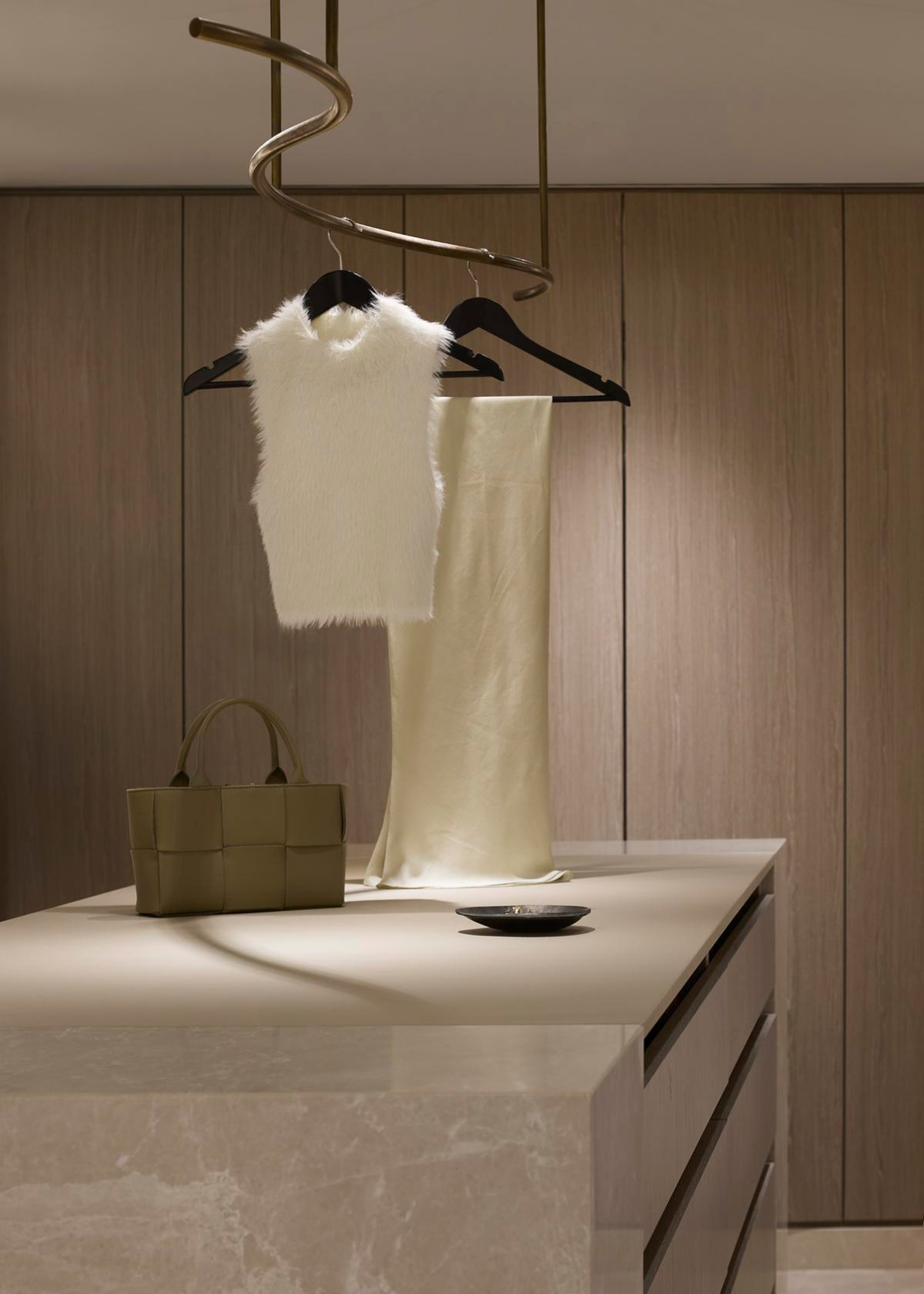 A minimalist walk-in wardrobe with a display rail above the closet island featuring a fuzzy sweater vest and a smooth skirt on black hangers