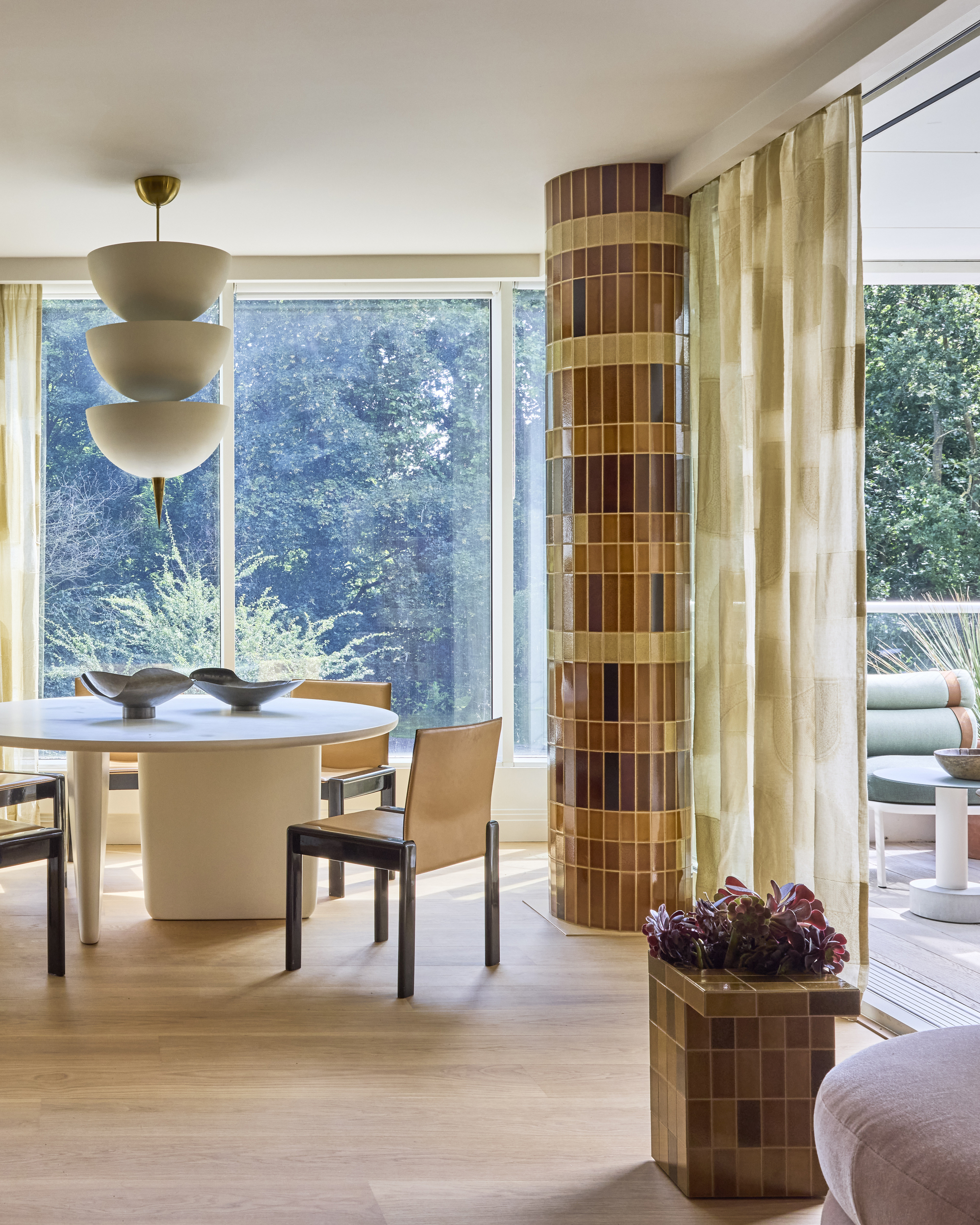 modern dining room with white ceiling, timber floors, tiled structural column, pendant over round white dining table and leather dining chairs with tiled side table