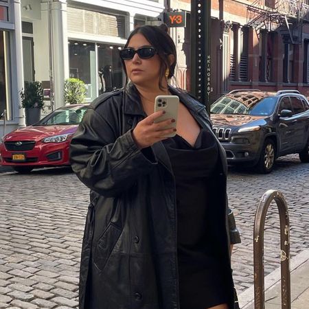 Woman wearing black leather coat, black dress, and black sunglasses standing on New York Street.