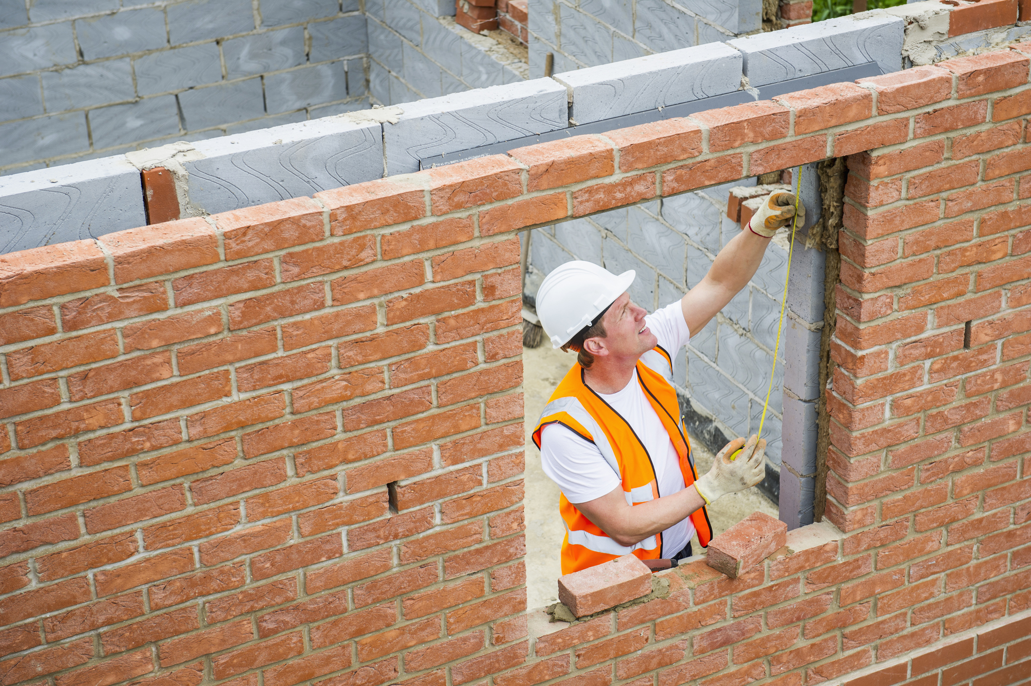 Construction worker laying bricks and using measuring tape