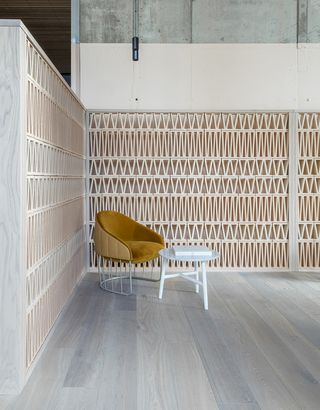 Leman Locke hotel. Geometrically placed wooden boards in the shape of a triangle are covering the walls. Ocher-colored suede chair sits in the corner, with a white table in front of it.