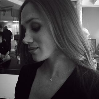 A black-and-white photo of Meghan Markle wearing a black top and a wishbone necklace looking down with her eyes closed