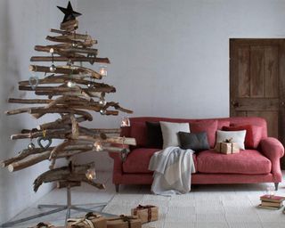 A Christmas tree made from wood logs and red upholstered sofa