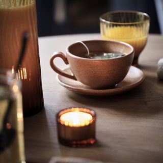 A cup of tea on a dining table with lit candles