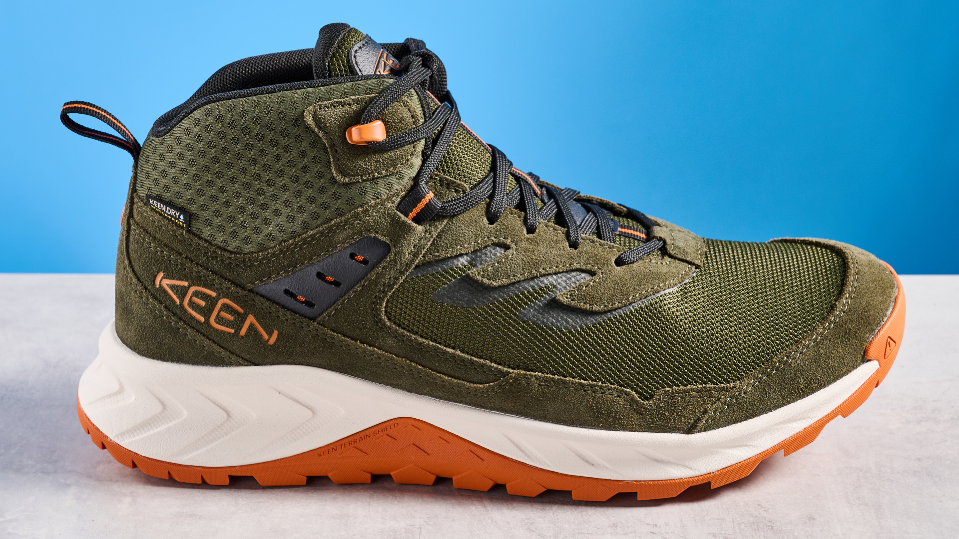 The Keen Hightrail Mid boots in Green on a stone surface against a blue background