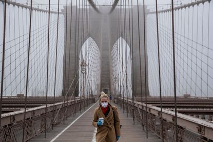  woman wearing a mask walks the Brooklyn Bridge in the midst of the coronavirus (COVID-19) outbreak on March 20, 2020 in New York City.