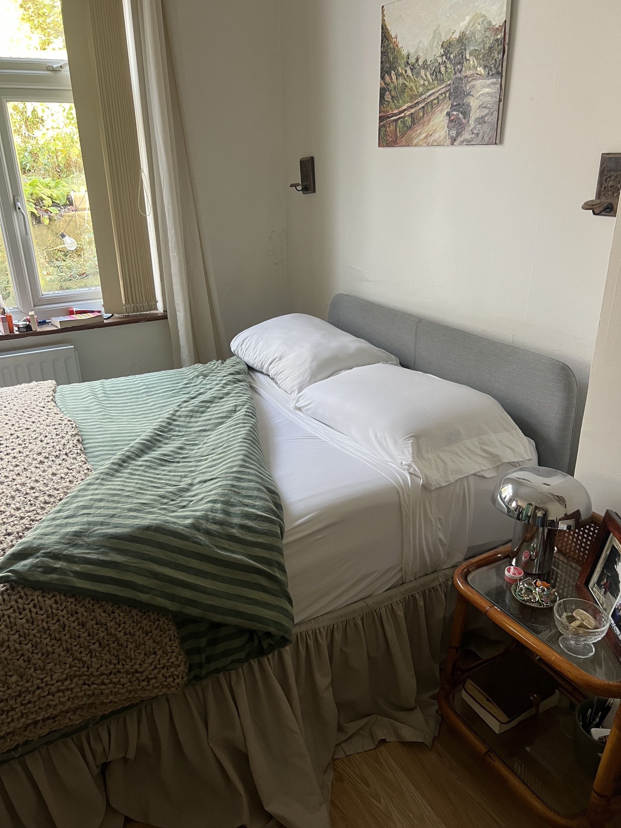 Image of a bed with a beige bed skirt, green striped bedding, and a knit throw. The bed is unmade to show white sheets.