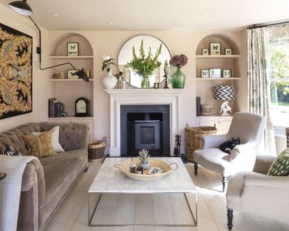 A neutral living room with marble fireplace, brown velvet sofa and two taupe armchairs