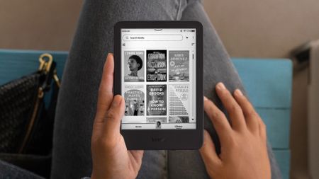 A woman holding a Kindle in her lap while sitting in a chair. 