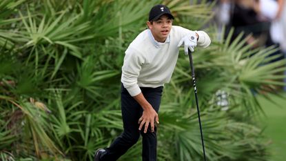 Charlie Woods holds his knee after hitting a drive