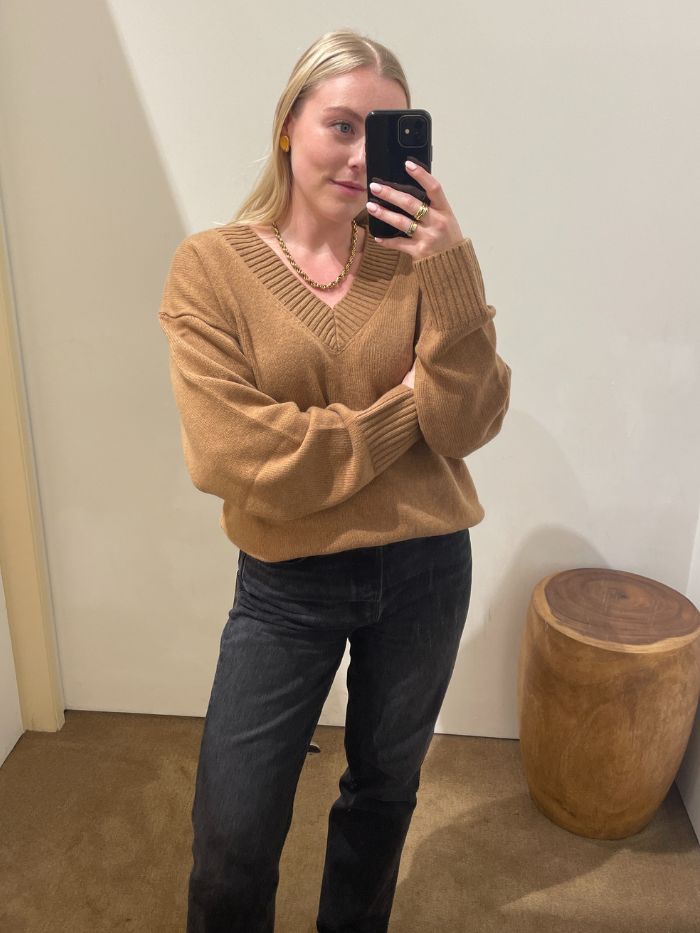 Woman wears camel cashmere jumper, black jeans and loafers